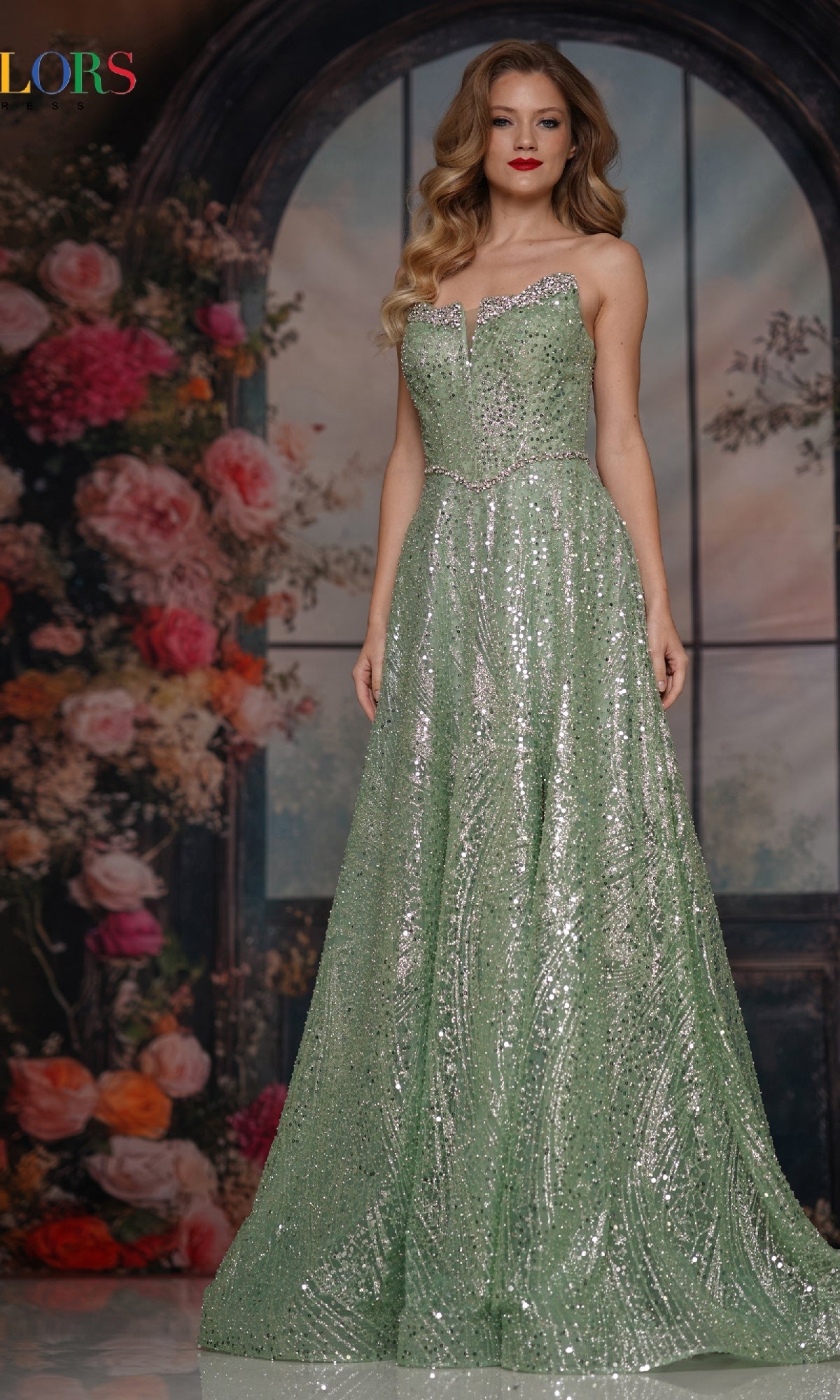 A woman poses before a floral backdrop in the Long Prom Dress: Colors Dress 3790, a floor-length, light green sequin gown featuring a sweetheart neckline and elegant strapless design.